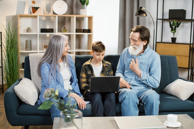 grandson-teaches-his-grandparents-use-laptop-sitting-sofa-living-room_161094-11674