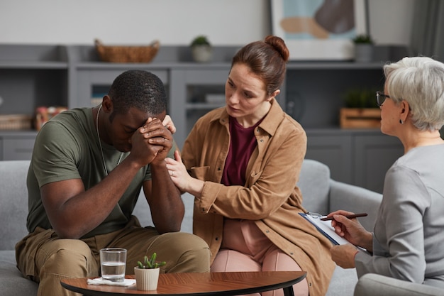 young-woman-supporting-depressed-african-man-while-they-visiting-psychologist_249974-7232